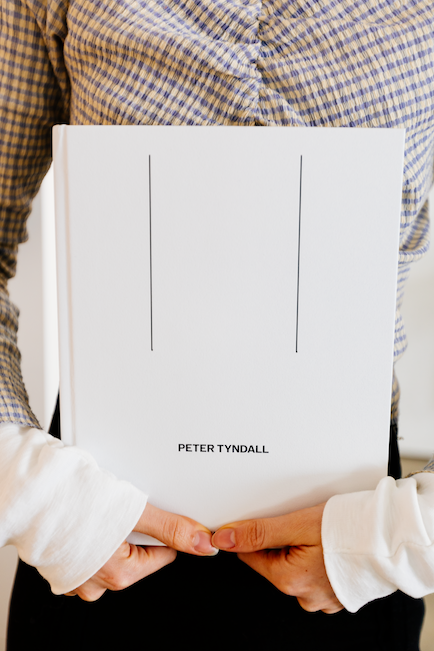 A woman holds the Peter Tyndall publication. It's a simple white cover with his name and two vertical lines.