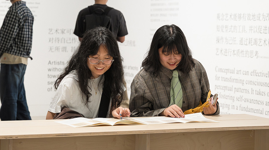 two women read publications at a table in a contemporary art space