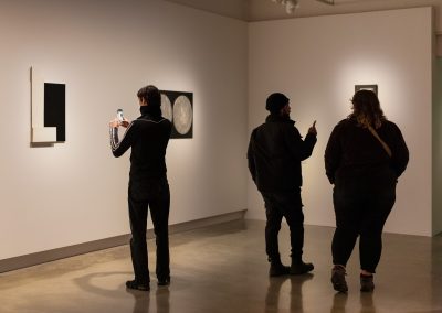 Three people take photographs on their phone of the artwork in the gallery