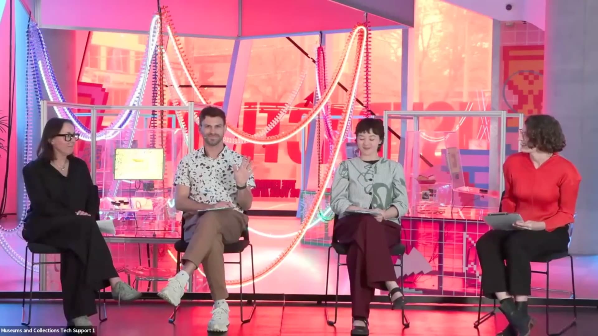 Four people sit on a stage with a bright pink background