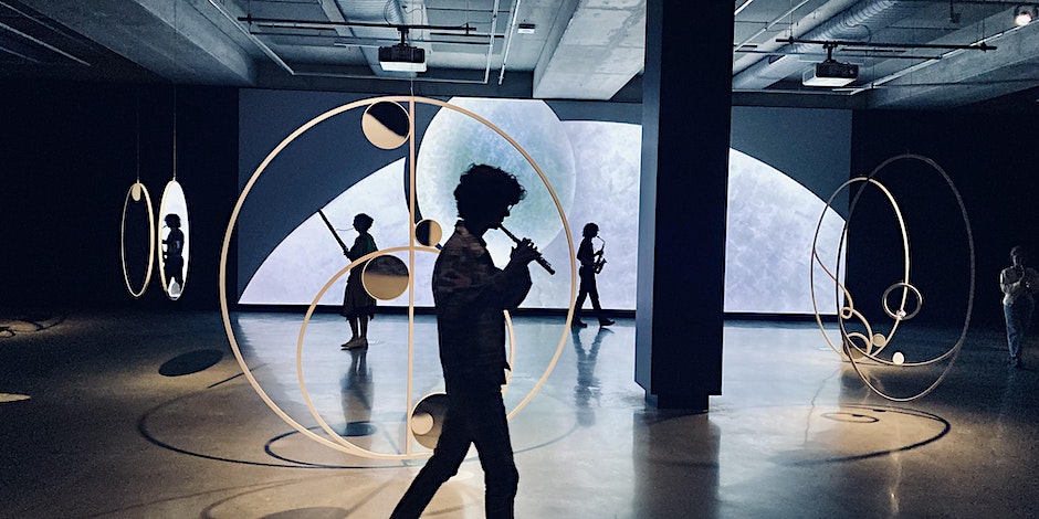 Three people in nightshifts walking in front of a video screen with a moon
