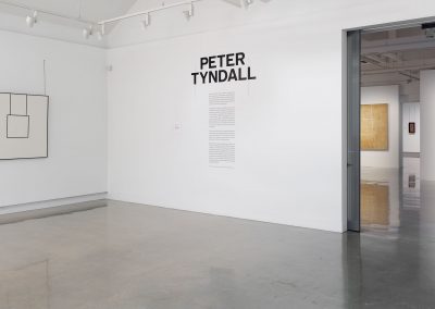 Entrance to the Peter Tyndall exhibition with an introducary text on a white wall with artworks in the background