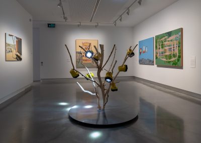a sculpture of torches in a tree with paintings on the surrounding gallery walls