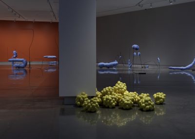 yellow blobs sit on floor in front of blue sculptures