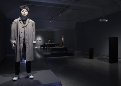 A lifelike human sculpture in an overcoat