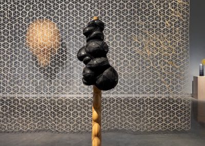 A black sculpture on wooden plinth with mesh screen behind
