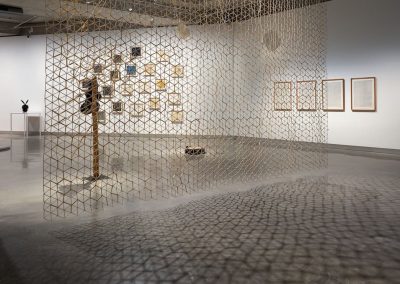 A series of artworks on a gallery wall with a mesh screen casting a shadow