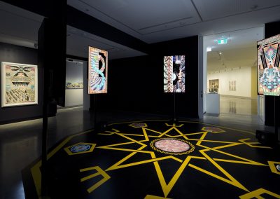A yellow star on the floor with artworks on black walls