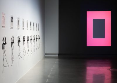 Headphones hang on a wall with a pink and grey rectangular artwork on the other wall