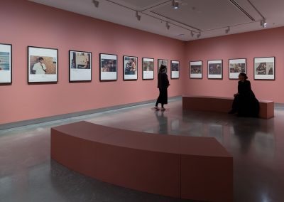 Artworks in a pink room with one visitor sitting on a pink bench