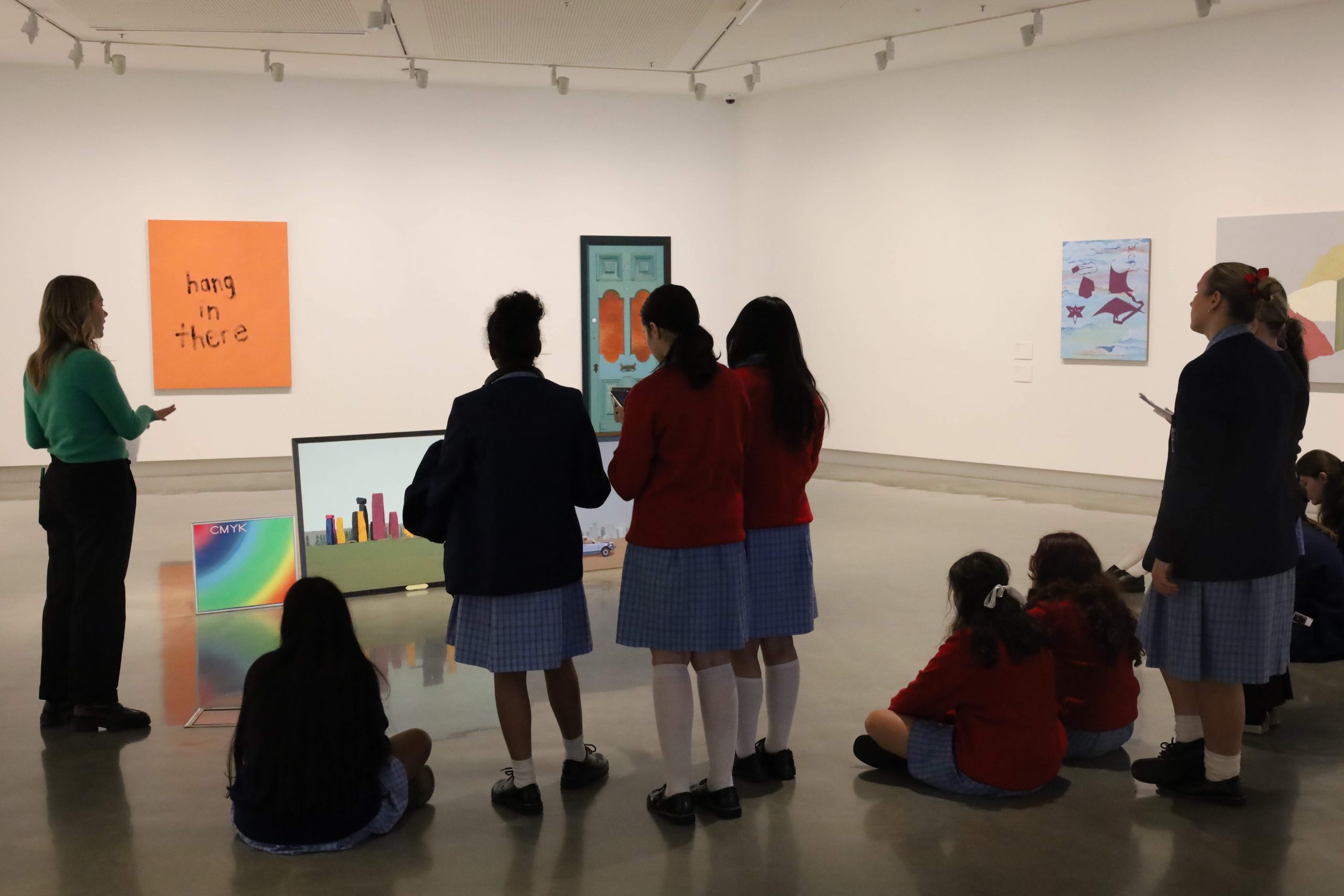 Students listen to a facilitator on a tour in Nadine Christensen's exhibitions of paintings.
