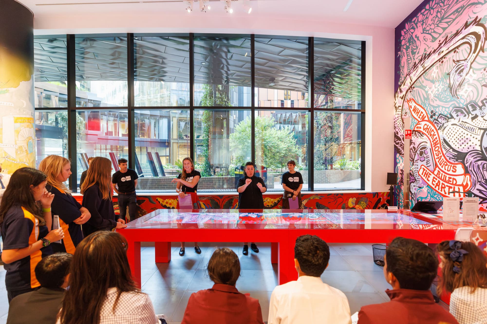 Students listen to educators at a red table in Science Gallery