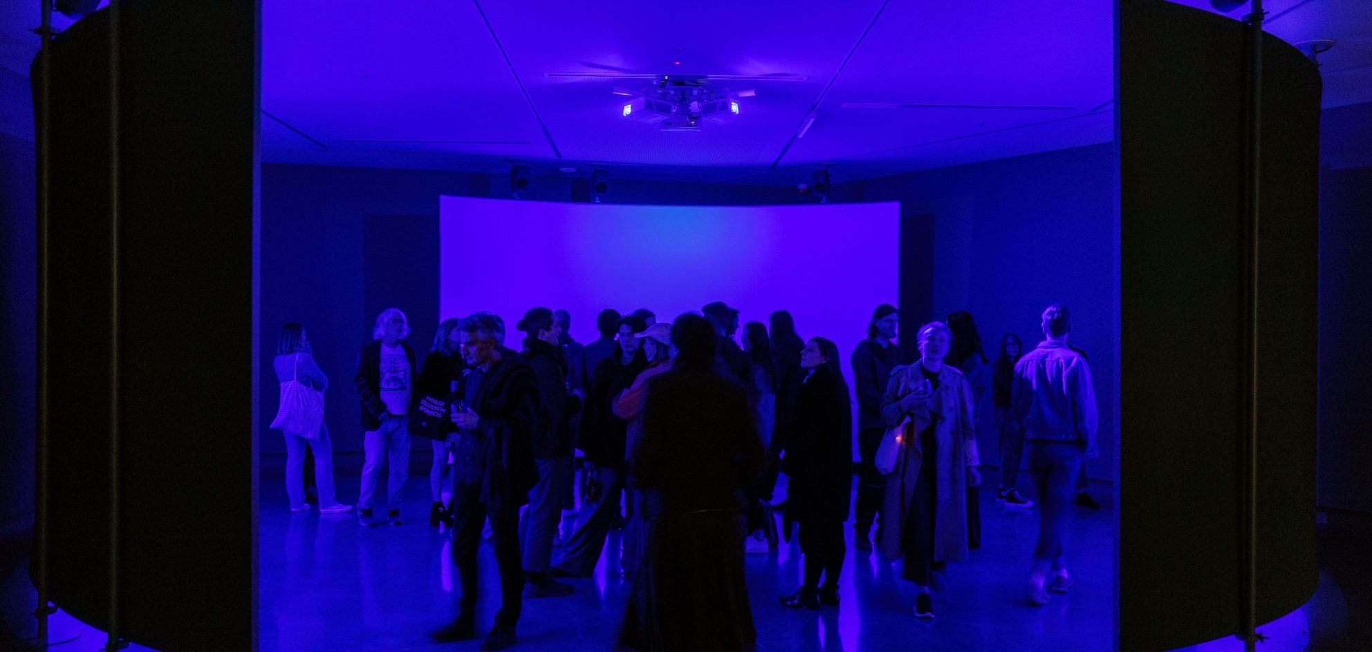 People move through darkened blue area at contemporary art gallery.