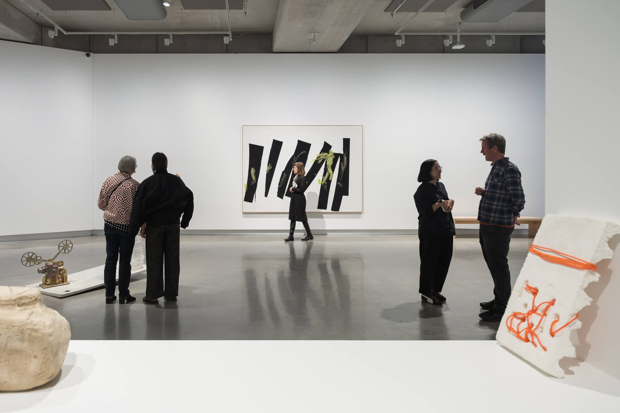 A group of figures stand in a white cube gallery.